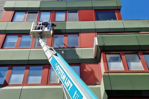 Hebebühne an einer mehrstöckigen Fassade mit roten Fensterrahmen