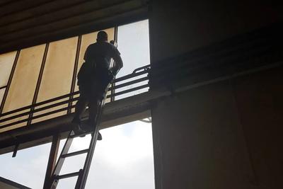 Mitarbeiter auf einer Leiter an hohen Hallenfenstern im Gegenlicht