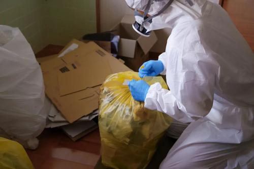 Mitarbeiter in Schutzanzug und Atemschutz verpackt Abfall in Säcke