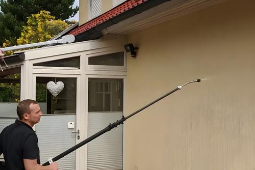 Mitarbeiter reinigt mit Teleskopstange an einem Wohnhaus