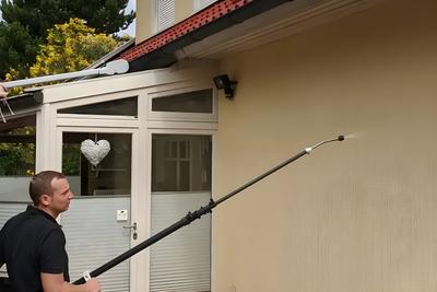 Mitarbeiter reinigt mit Teleskopstange an einem Wohnhaus