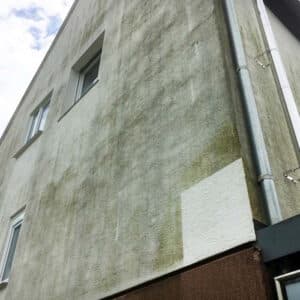 Eine dreckige Hausfassade. Eine kleine viereckige Fläche ist sauber, da die Fassadenreinigung an einer Probefläche ausprobiert wurde.